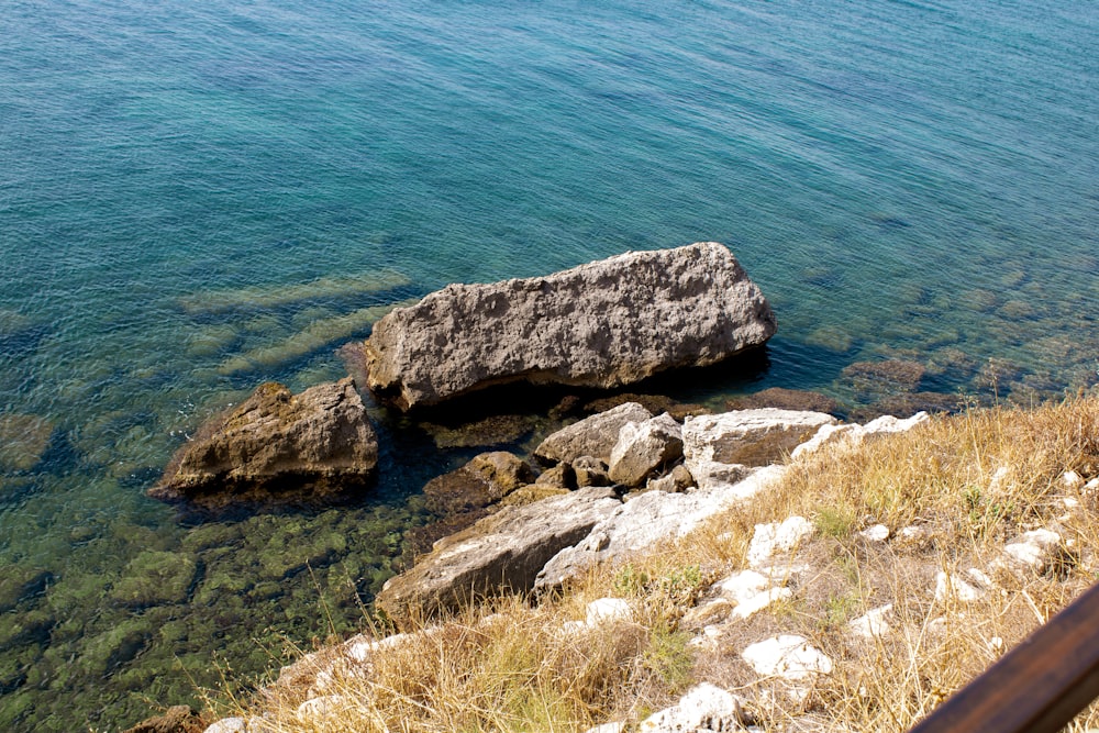 a large rock sitting on top of a lush green hillside next to the ocean