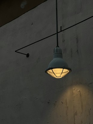 A single industrial-style wall-mounted lamp casts a warm glow against a textured concrete wall, creating a subtle play of light and shadow.