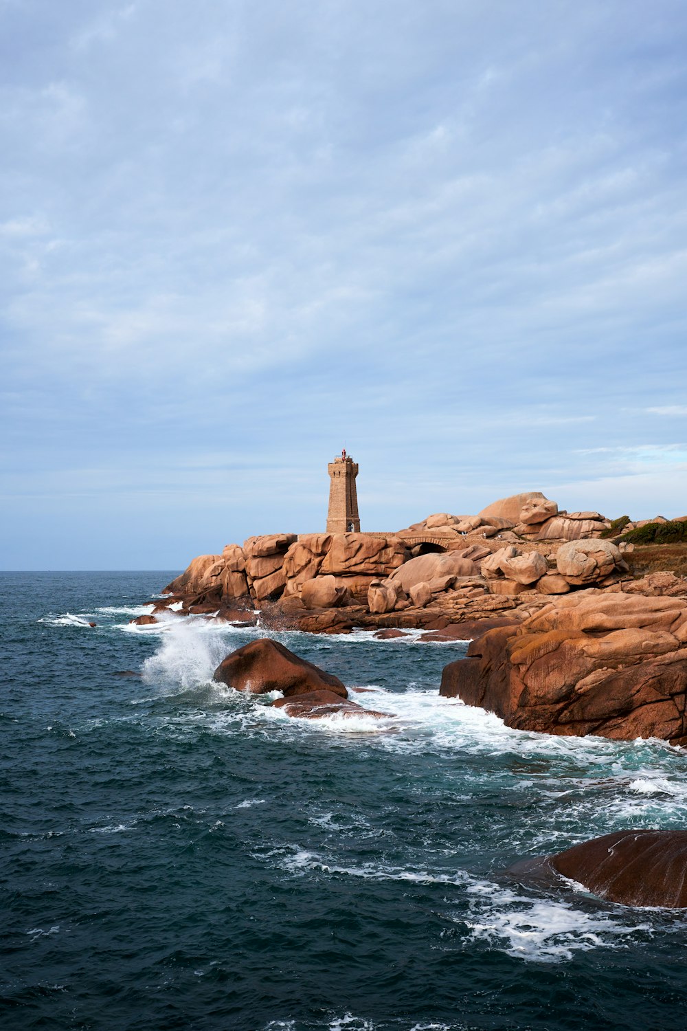 a lighthouse on a rocky shore with a body of water in the foreground