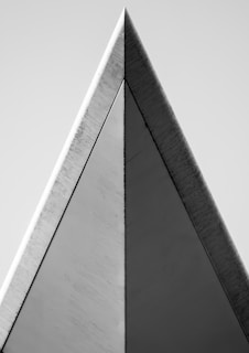 A monochrome architectural image featuring a sharp triangular structure with clean lines and contrasting surfaces. The geometric design emphasizes symmetry and minimalism.