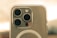 A close-up view of a smartphone camera, featuring three large lenses and a smaller circular flash component. The phone's back appears to be encased in a clear protective cover. The lighting is warm, suggesting a golden hour or soft lighting environment.