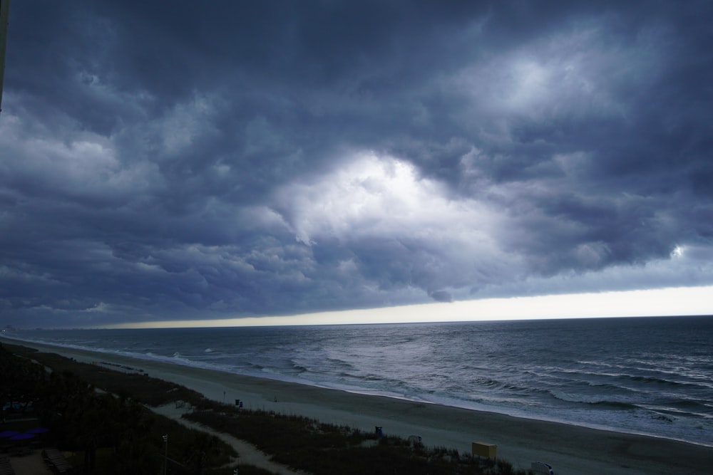 a dark cloudy sky over the ocean with a beach in the foreground