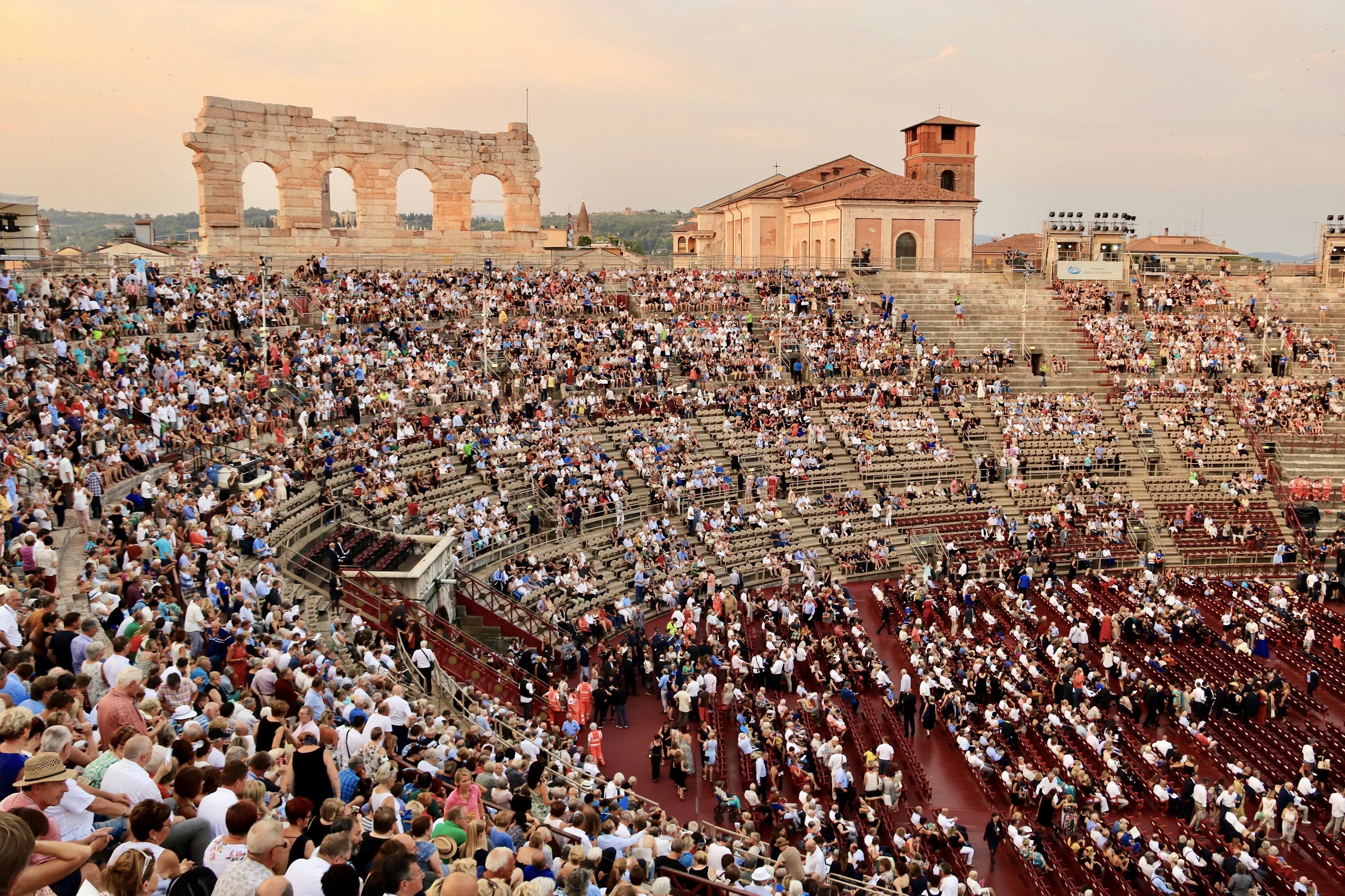 A packed crowd fills the ancient Verona Arena's stone tiers at golden hour for an open-air opera night.
