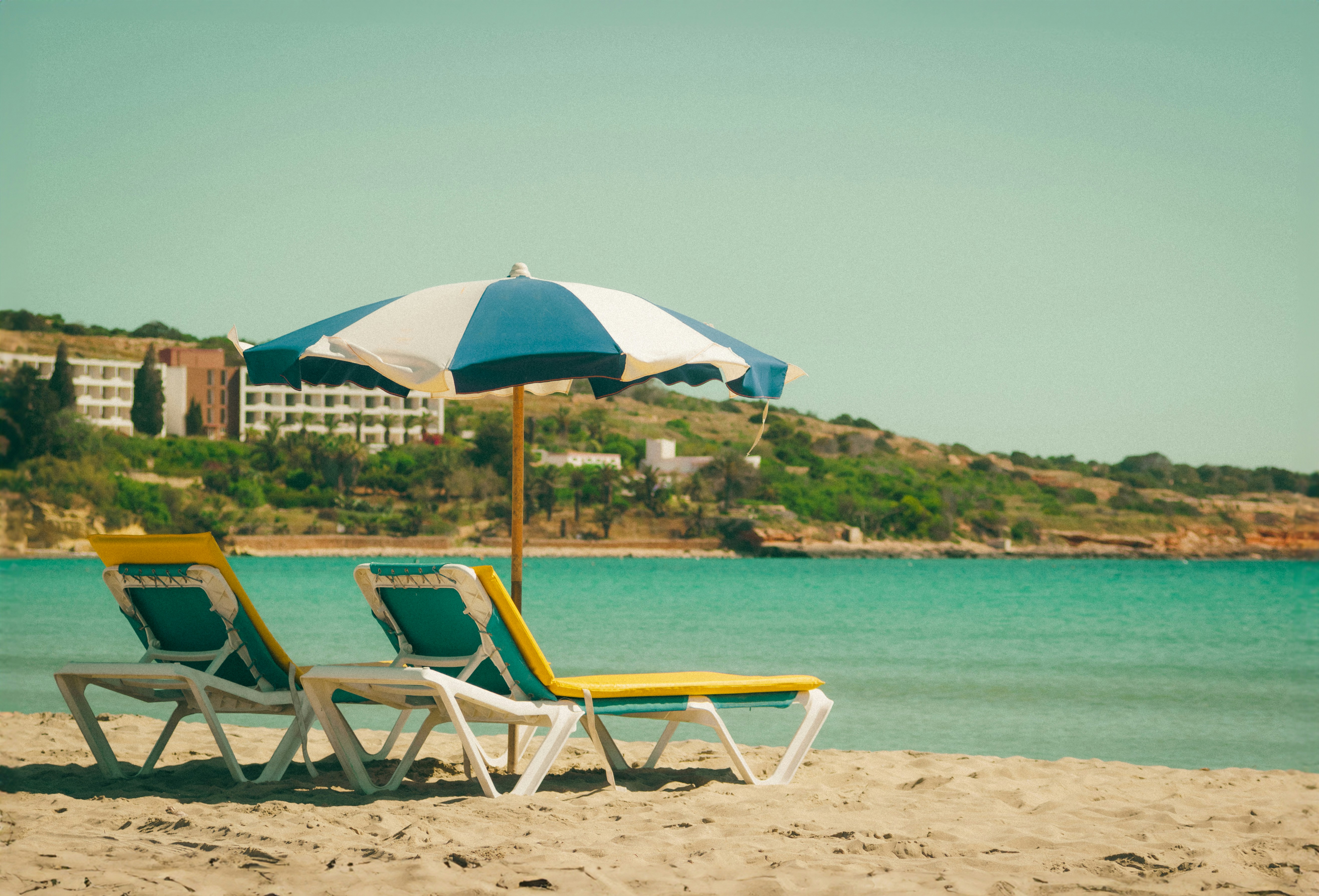 a couple of lawn chairs sitting on top of a sandy beach, 