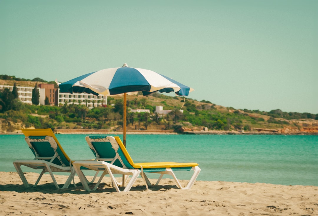 a couple of lawn chairs sitting on top of a sandy beach,