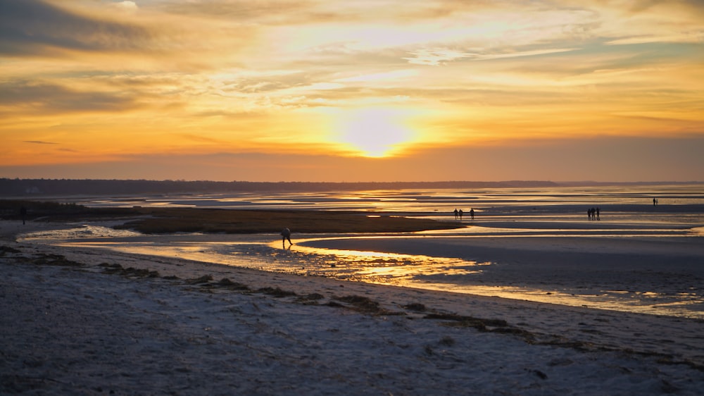 the sun is setting over the beach and people are walking