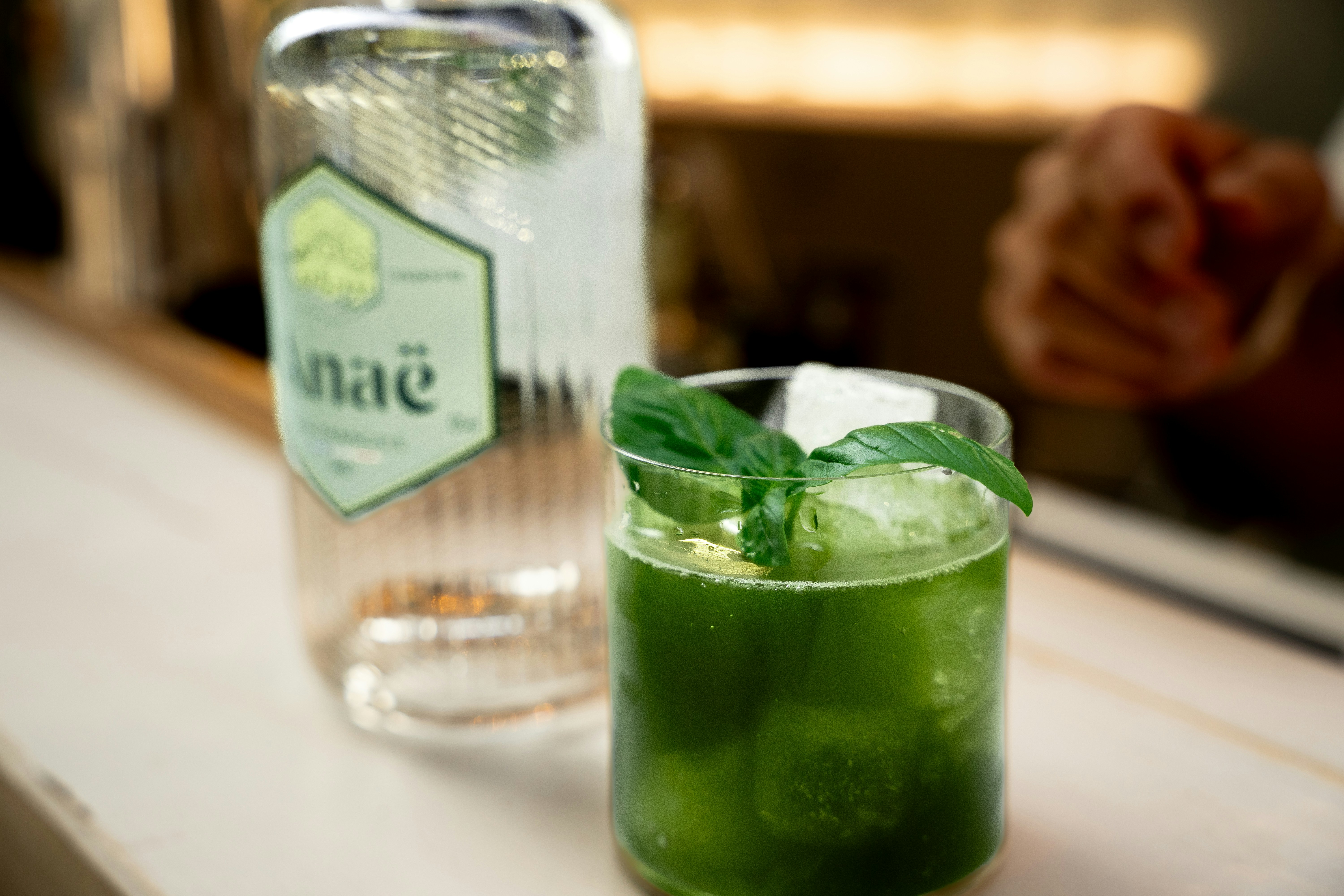 a close up of a drink on a table, basil Smash X Anaë Gin Cocktail réalisé à base de sirop de basilic maison et de Gin AnaÊ en plus de sa clear Ice