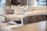 A modern living room featuring a plush cream-colored sectional sofa with several cushions. A decorative chess set is placed on a small table in the background, adding a sophisticated touch. Soft natural light filters through the space, creating a serene atmosphere.