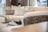 A modern living room featuring a plush cream-colored sectional sofa with several cushions. A decorative chess set is placed on a small table in the background, adding a sophisticated touch. Soft natural light filters through the space, creating a serene atmosphere.