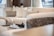 A modern living room featuring a plush cream-colored sectional sofa with several cushions. A decorative chess set is placed on a small table in the background, adding a sophisticated touch. Soft natural light filters through the space, creating a serene atmosphere.