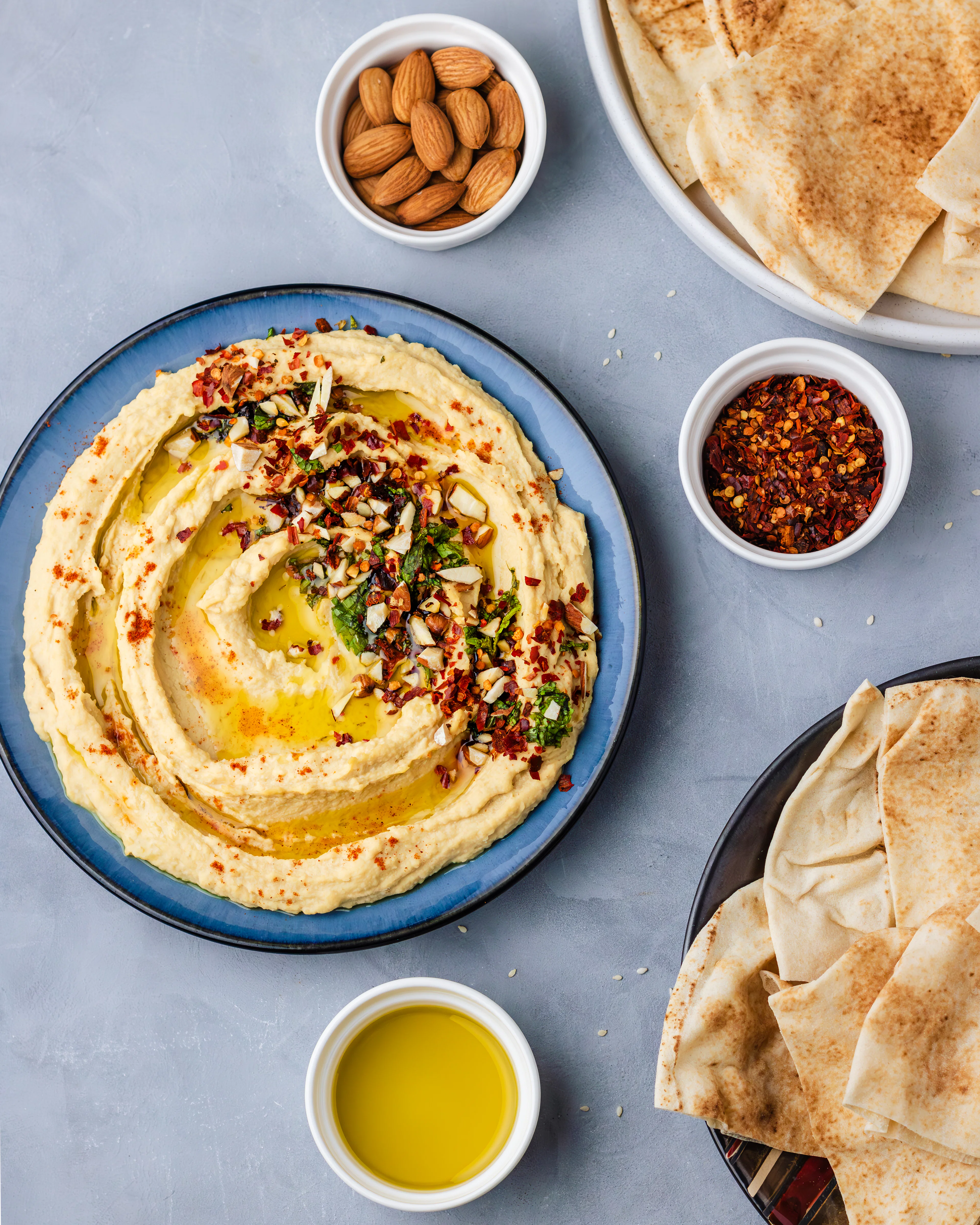 Swirled hummus with olive oil, chilli flakes and herbs on a blue plate with pita
