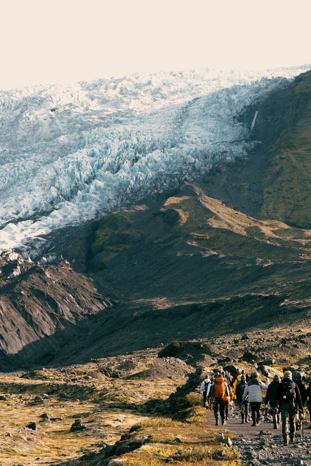 a group of people walking up a hill towards a glacier