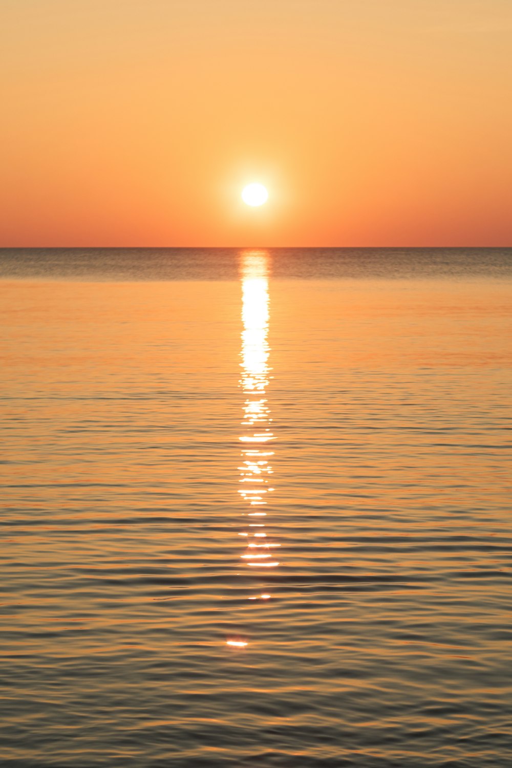 the sun is setting over the ocean with a boat in the water