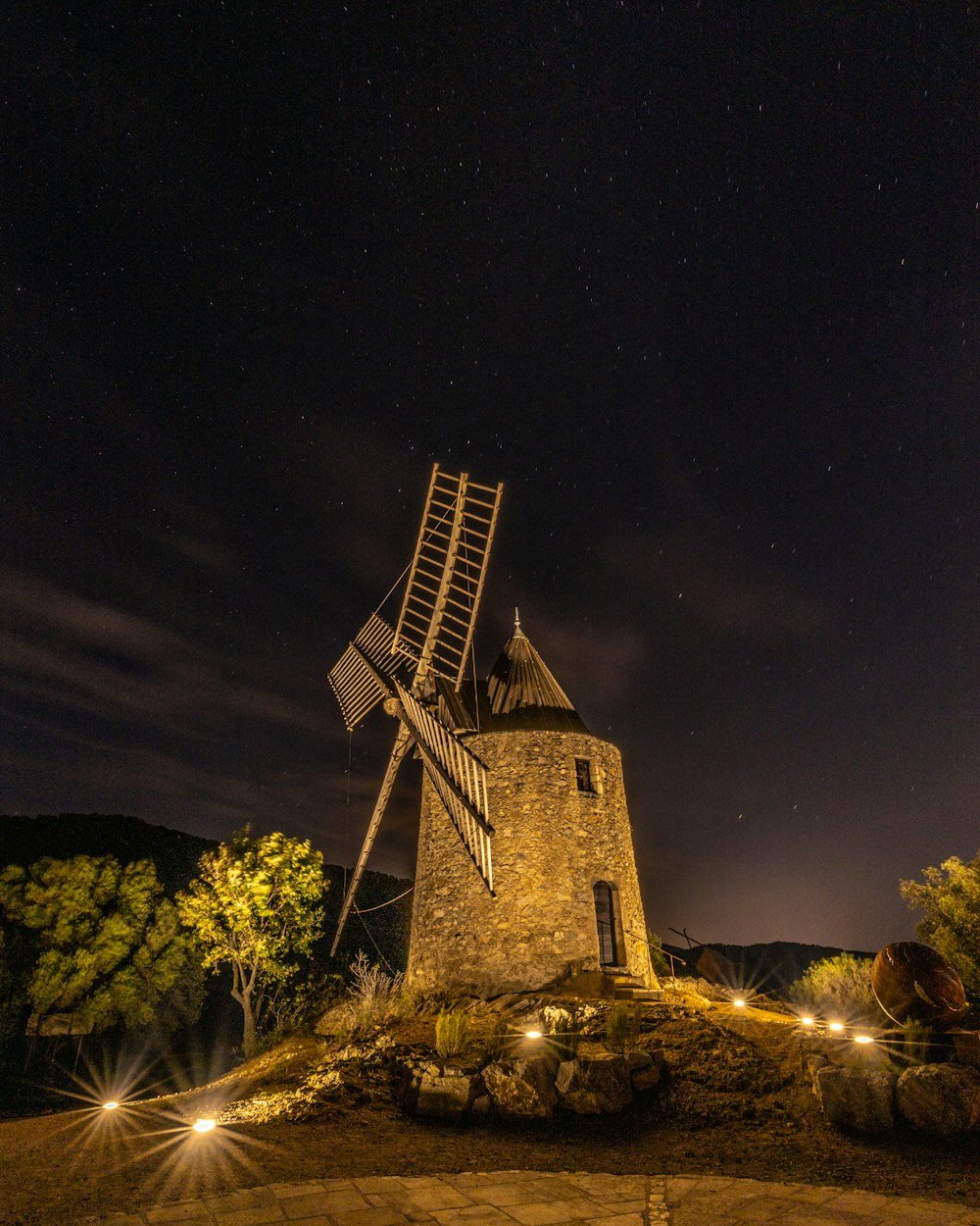 um moinho de vento sentado no topo de uma colina à noite