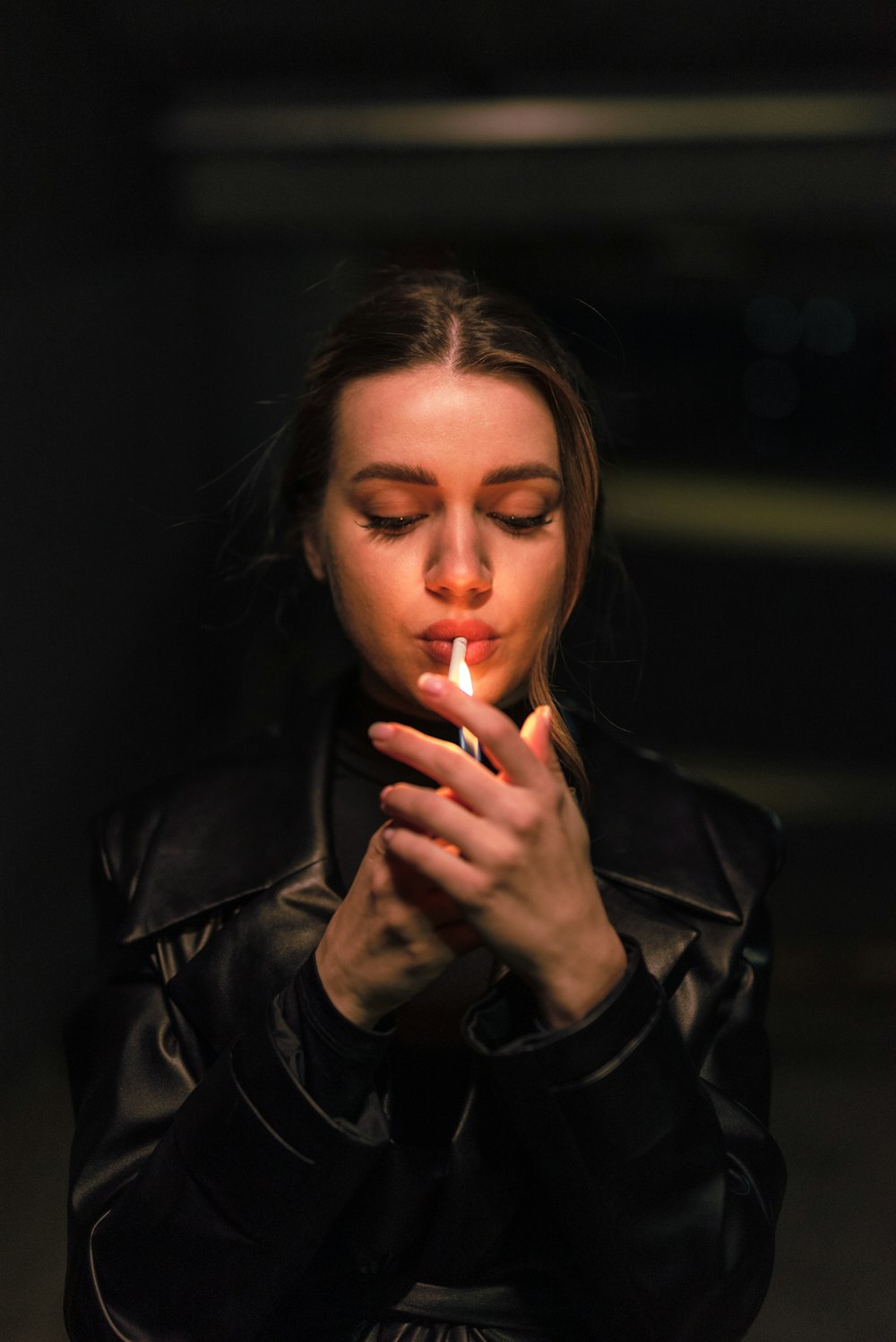 a woman in a black leather jacket lighting a cigarette