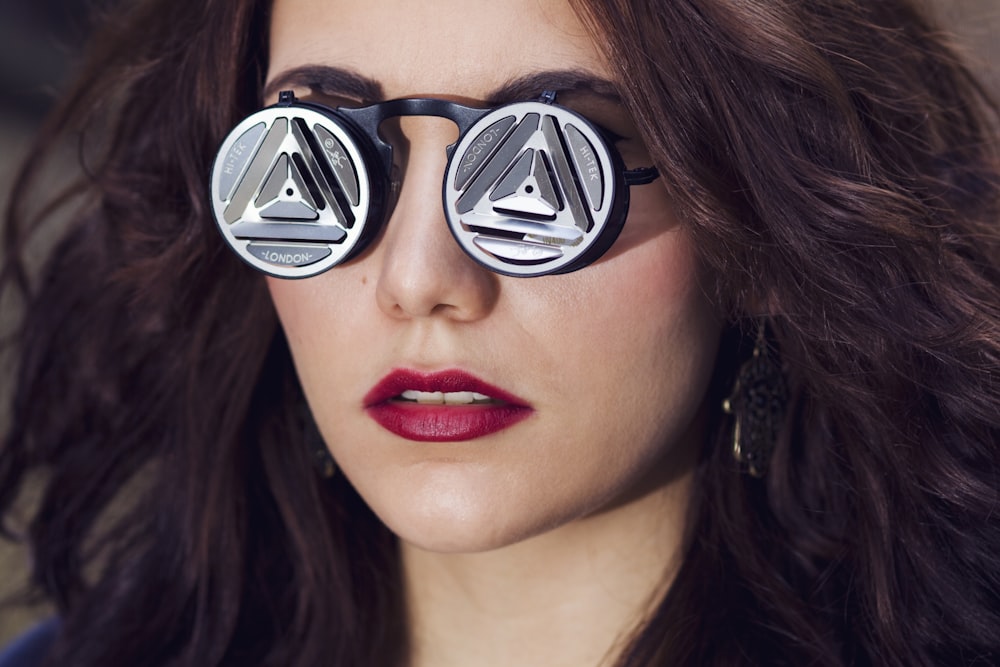 a woman with dark hair and red lipstick wearing round sunglasses