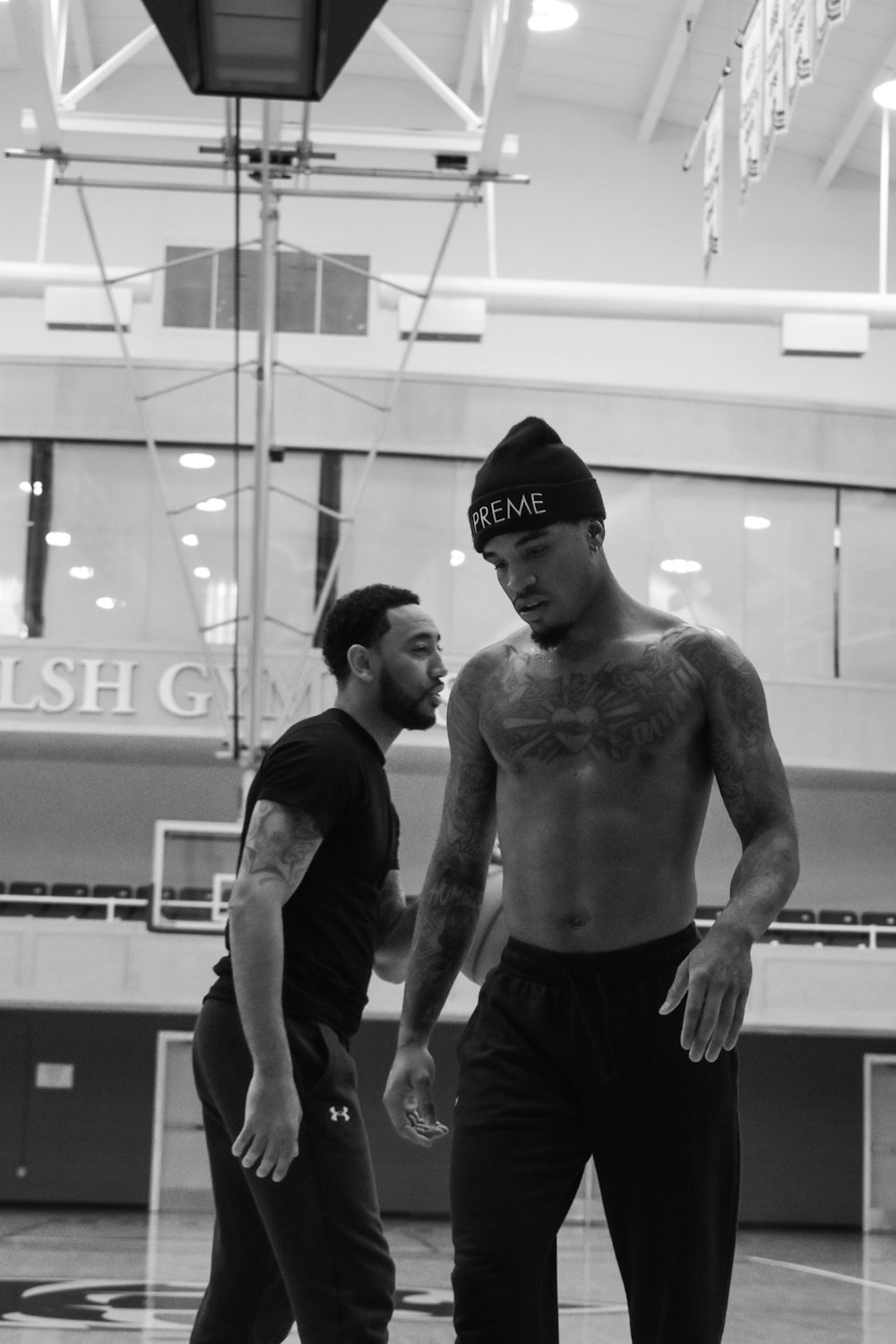 a shirtless man standing next to another man on a basketball court