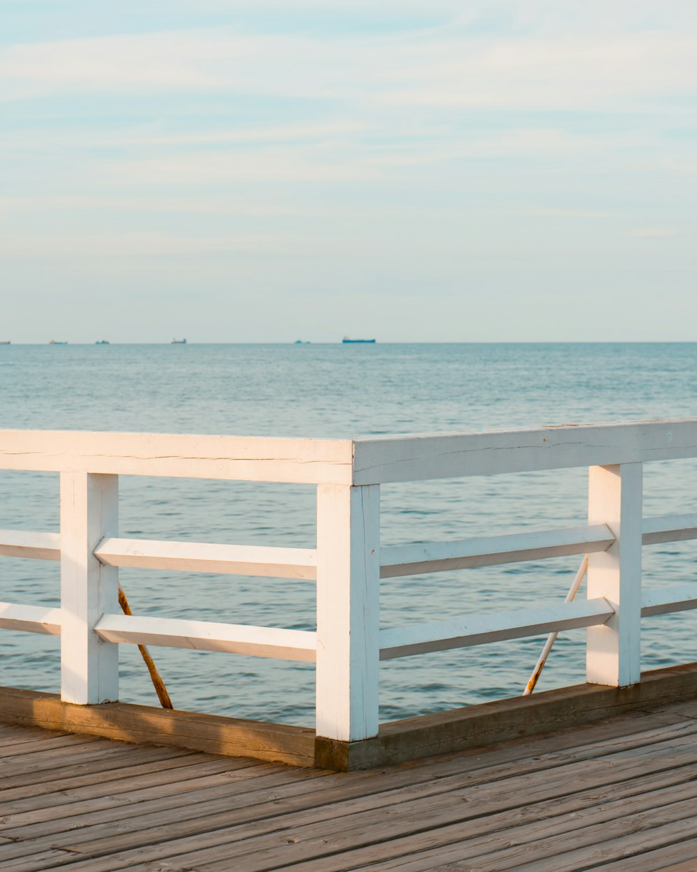 a wooden pier with a white railing next to the ocean
