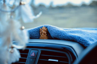 Close-up of a hand placing a bright ceramic car perfume diffuser on a dashboard surrounded by soft fabric textures.