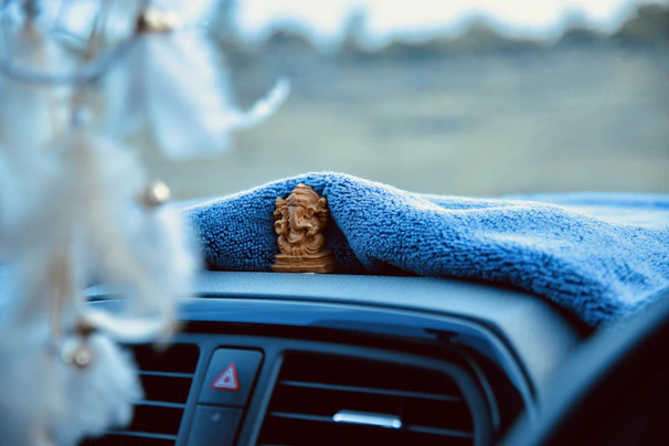 Close-up of a hand placing a bright ceramic car perfume diffuser on a dashboard surrounded by soft fabric textures.