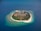 A small, lush island surrounded by vibrant turquoise waters and a coastline of white sandy beaches. The island features a dense cluster of buildings and vegetation in the center, with clear water extending into the deep blue ocean.