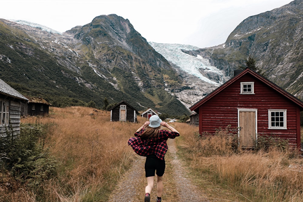 a woman walking down a dirt road next to a red building