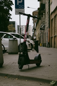 A compact electric scooter parked by a city sidewalk under soft sunlight.