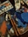 A painter's workspace featuring a palette covered with various shades of blue and some red paint. There are several brushes, some with paint on their bristles, and tubes of paint in the background. An open paint palette shows remnants of mixed colors.