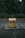 A yellow recycling bin with signage stands on a cobblestone path, surrounded by dense green foliage and trees in the background. The bin appears to be in a park or wooded area.