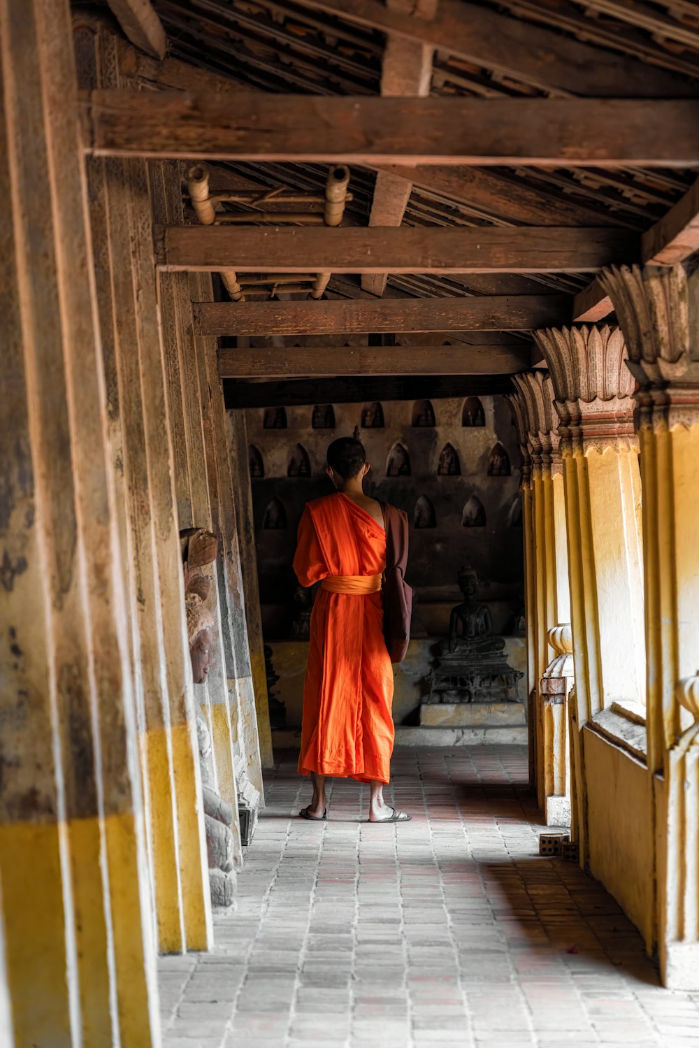 a monk in an orange robe walking down a hallway