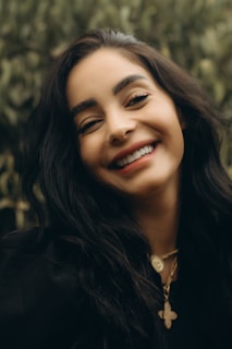 A woman wearing a pendant necklace, smiling in a natural outdoor setting.