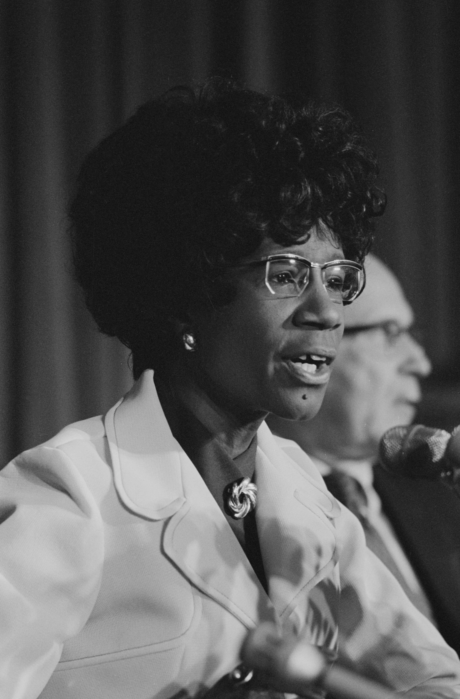 Congresswoman Shirley Chisholm speaking into a microphone during a public address.