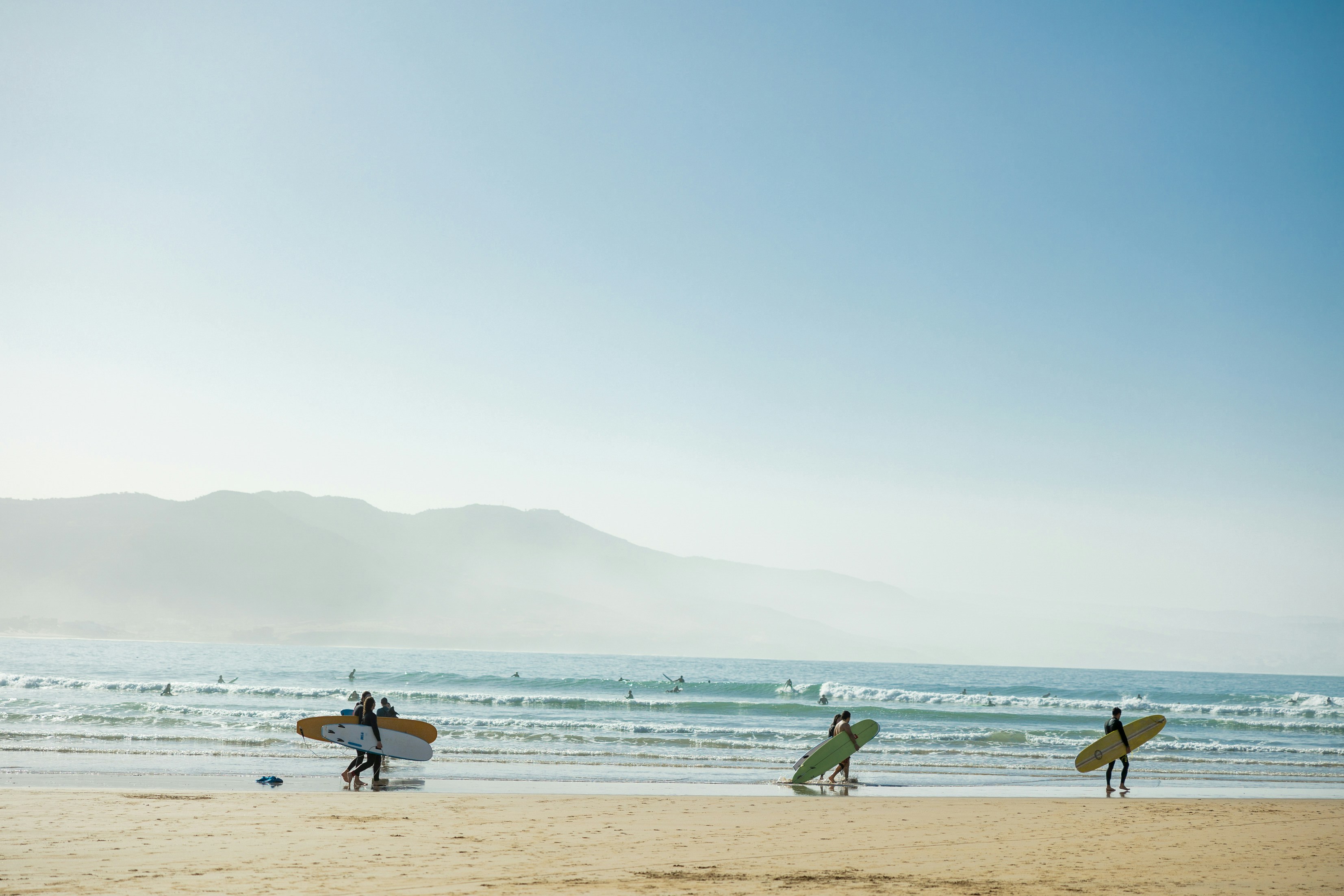 a group of people carrying surfboards on top of a beach