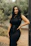 A stylish woman wearing a minimalist black dress from noirluxe, smiling outdoors.