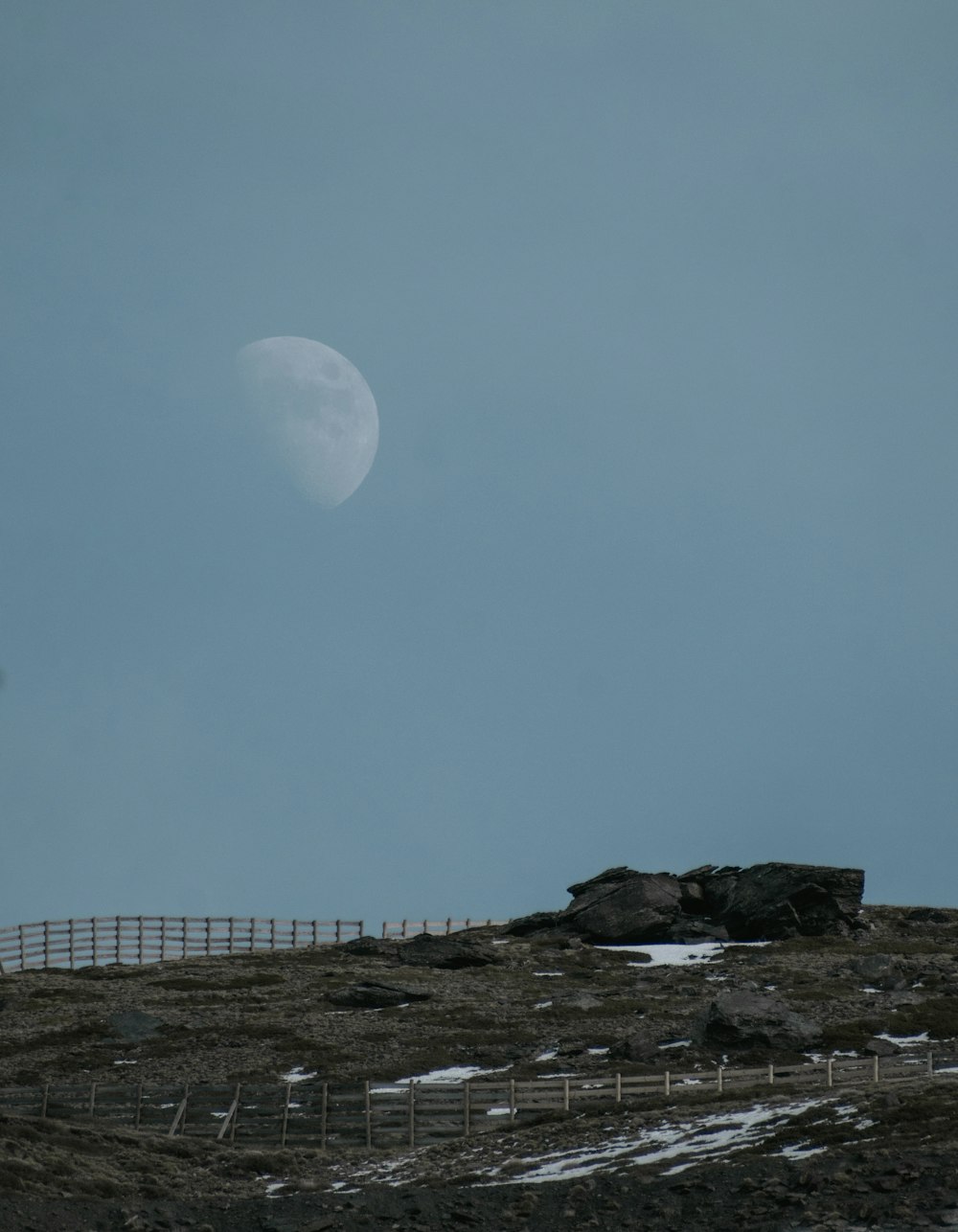 uma lua cheia é vista sobre uma cerca no topo de uma colina