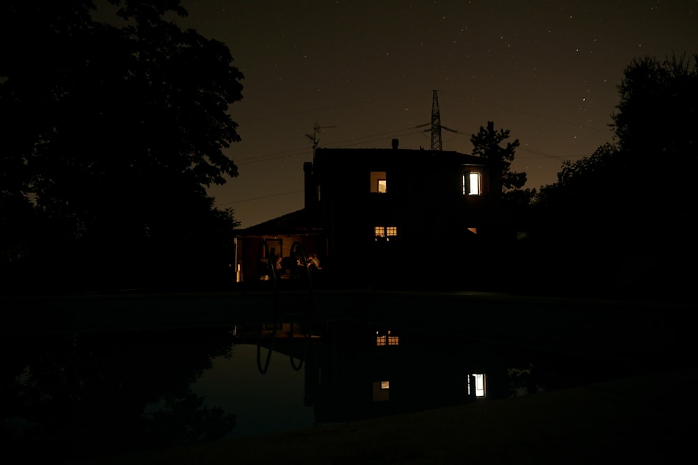 a house is lit up at night with a reflection in the water