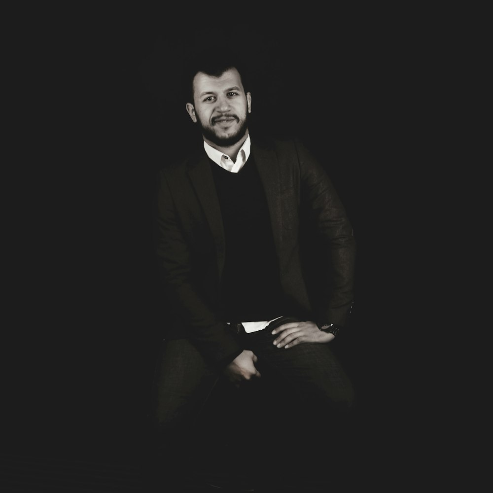 a man sitting in a dark room with his hands in his pockets