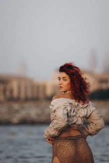a woman with red hair is standing by the water