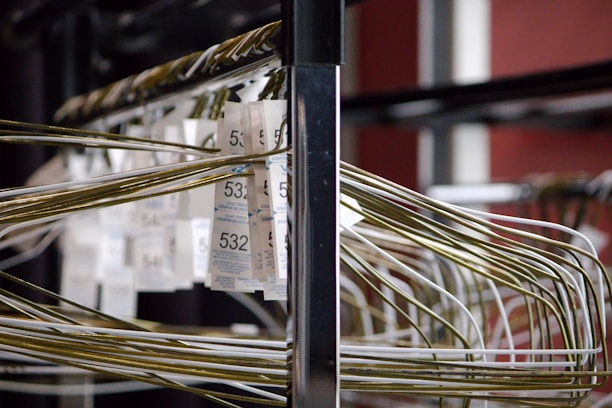 A close-up of a coat check rack filled with metal hangers and white claim tickets, each displaying a number in bold. The scene is indoors, with a focus on the parallel alignment and intersecting lines created by the hangers.