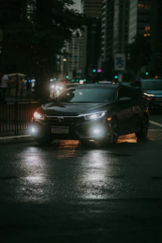 A sleek black sedan parked under city lights at dusk