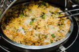 Steaming bowl of rich, aromatic biryani garnished with herbs and fried onions.