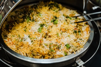 A large serving dish filled with fragrant biryani garnished with fresh cilantro. The dish showcases a colorful mix of rice, spices, and vegetables, with traces of white, yellow, and green hues throughout.