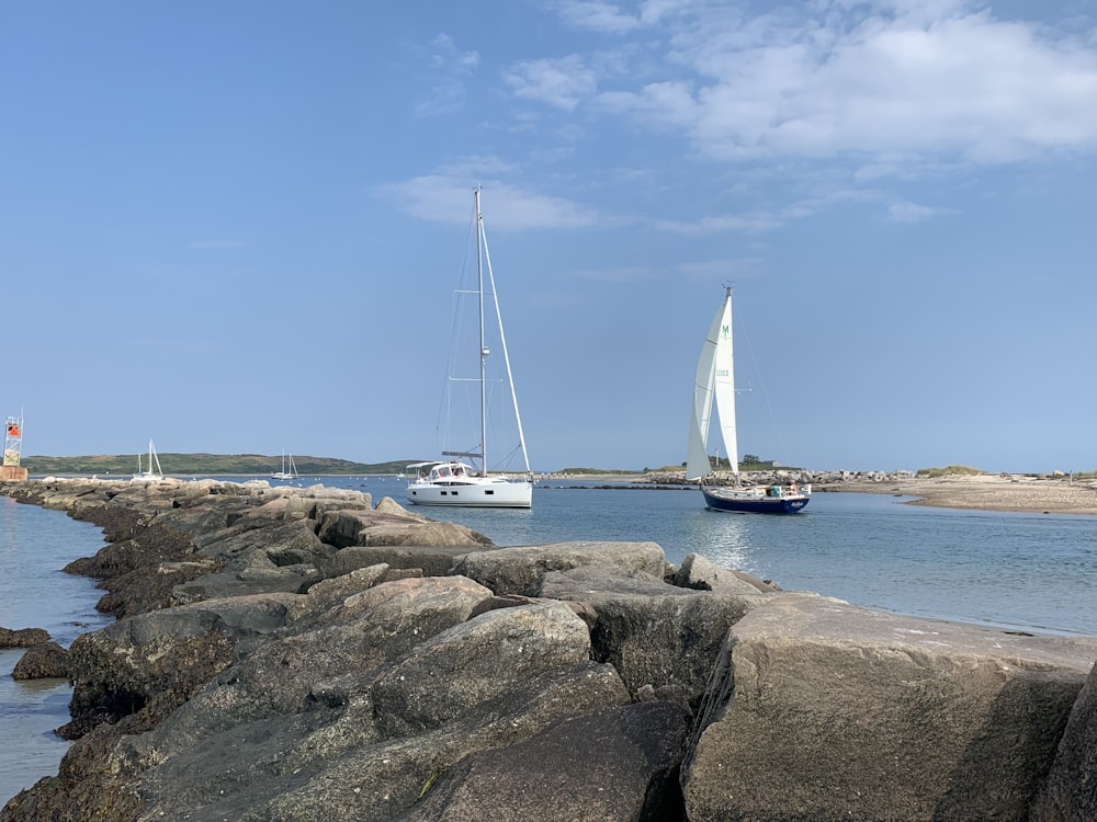 two sailboats on the water near a rocky shore