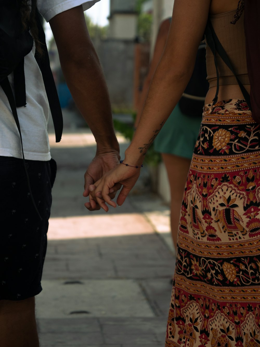 a man and woman holding hands walking down a sidewalk
