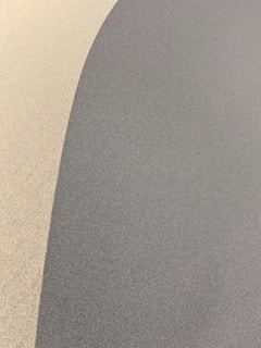 A minimalist scene with a smooth, curving line separating two differently shaded areas. The left side features a light, sandy texture, while the right side is a darker gray shade. The soft gradient and gentle curve create a sense of depth and movement.