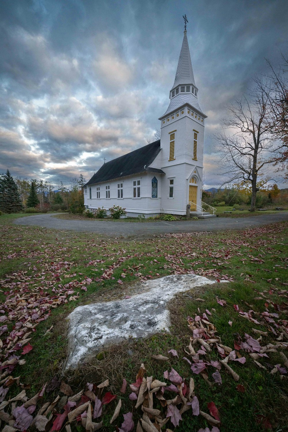 a white church with a steeple surrounded by fallen leaves
