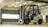 A forklift is situated in an indoor garage or warehouse environment. It is a Nissan model with a large lift mechanism and the designation 'B38' on its side. The area is well-lit with fluorescent lights, and a large industrial-style window is visible in the background along with concrete beams and walls.