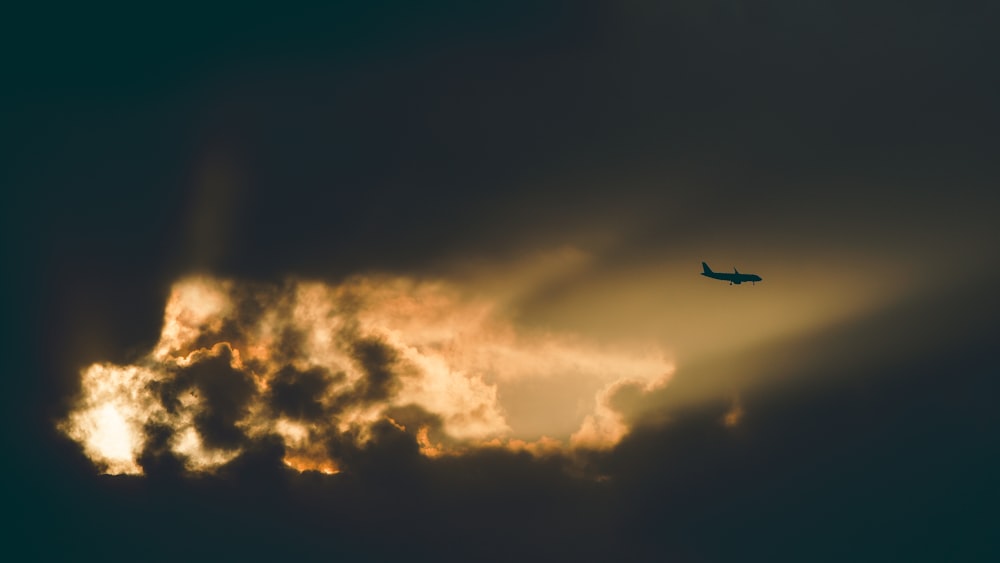 um avião voando através de um céu nublado ao pôr do sol