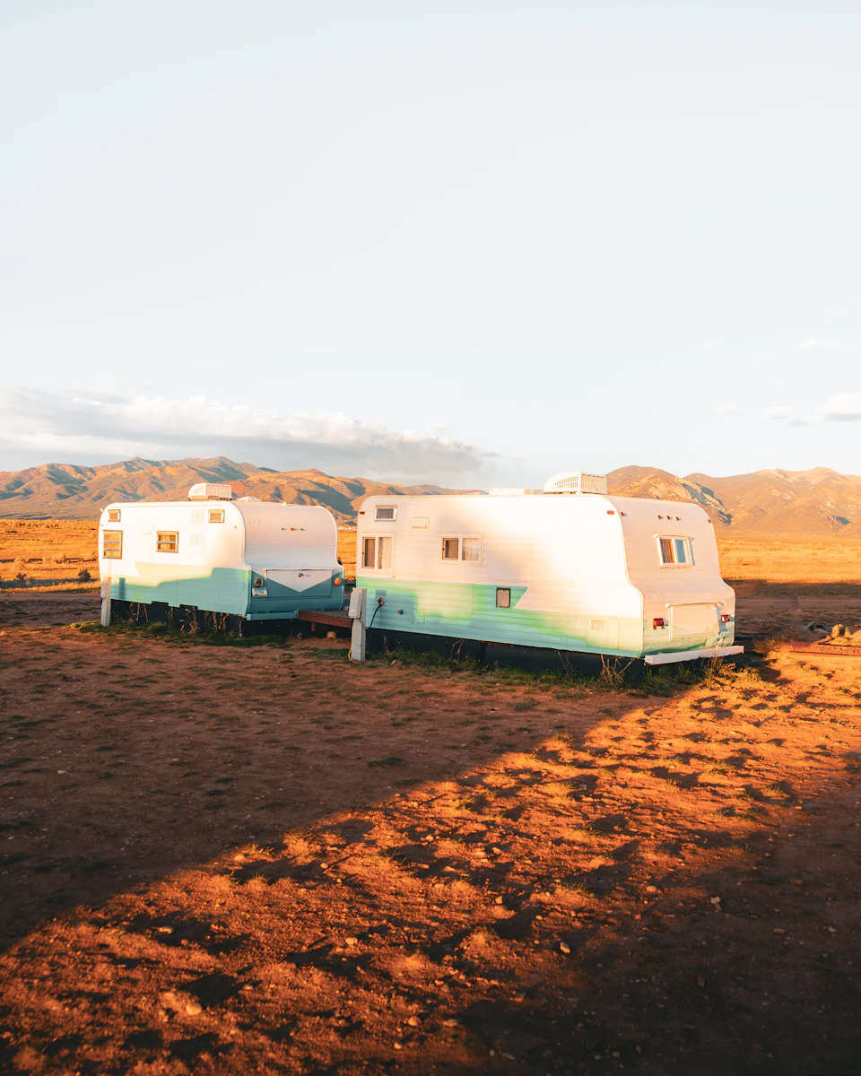 Two vintage camper trailers face each other on a dirt road amidst majestic mountains