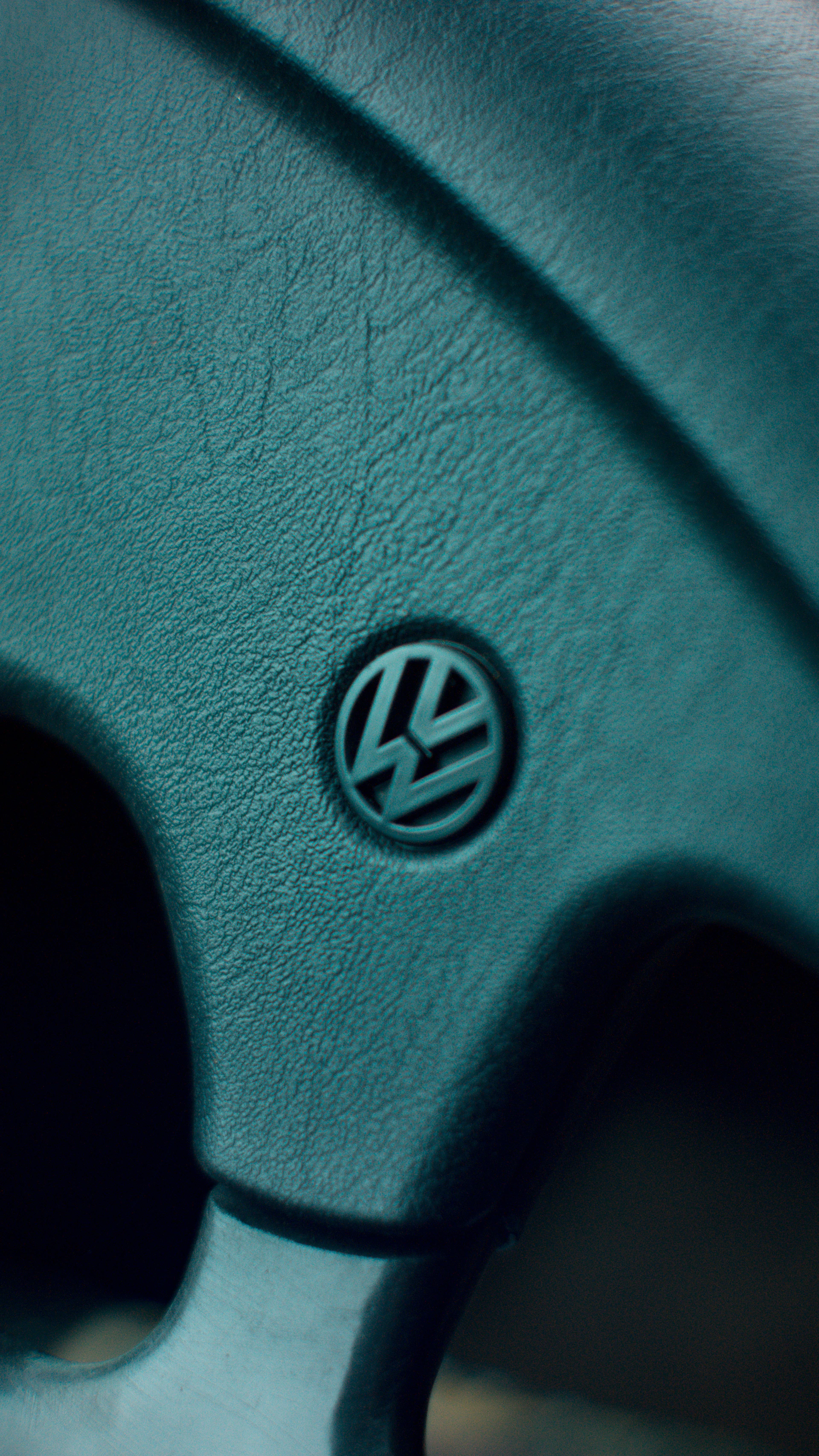 Detailed shot of a bespoke steering wheel wrapped in fine leather with subtle aqua stitching, set against a minimalist black and white background.
